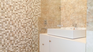 A bathroom with a tiled mosaic wall, a white sink, and a marble-tiled shower area.