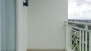 A balcony with a white railing, a small black wall-mounted light fixture, and a view of a cityscape.