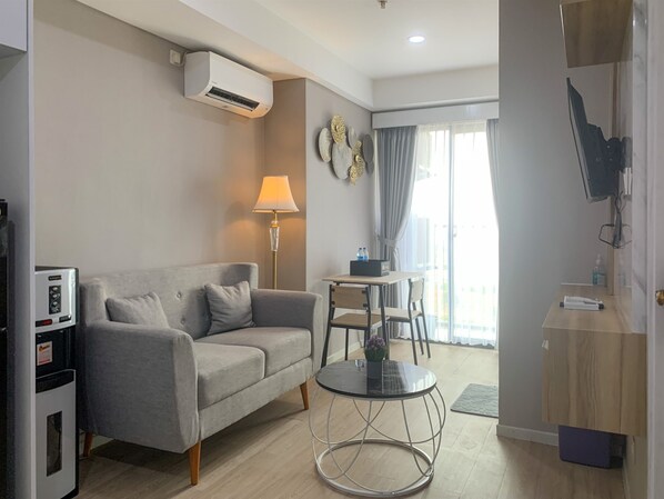 A modern living room with a grey sofa, a small round table, a lamp, and a TV mounted on the wall.