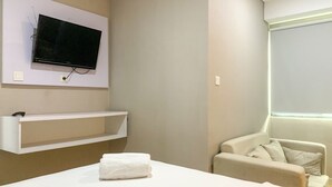Una camera d'albergo con un letto, una TV a muro, un piccolo ripiano, una finestra e una sedia.