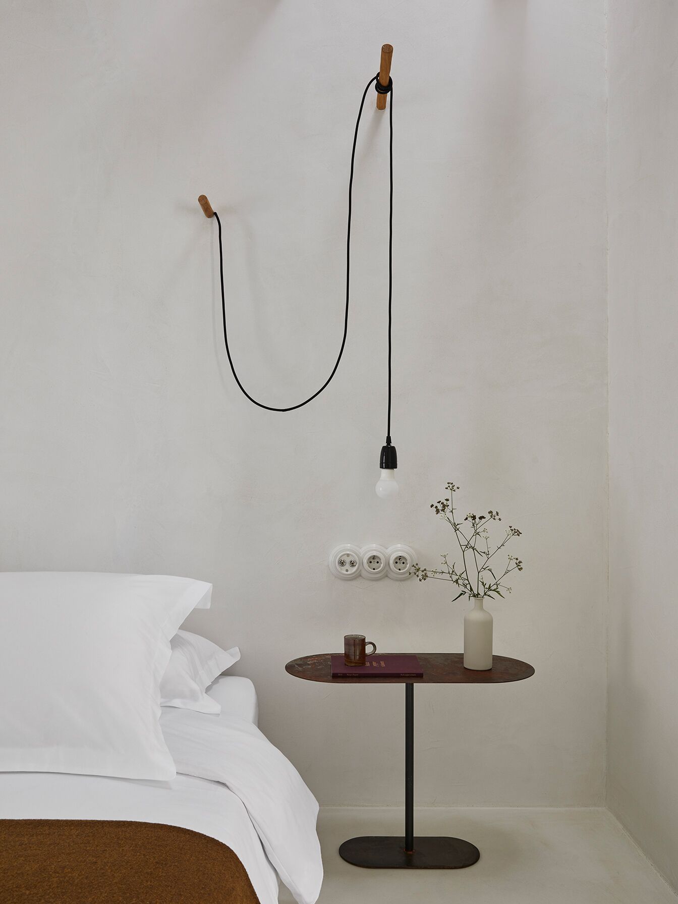 Une pièce comprenant un lit, une petite table ronde avec un vase et une tasse, et une lampe de sol à col flexible.