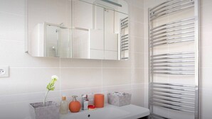 A modern bathroom with a white tiled wall, a glass shower enclosure, a white countertop with a sink, and a towel rack. - La Croisette - One Bedroom Apartment, Sleeps 4 (Cannes)