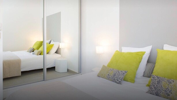 A modern hotel room with a large bed, a bedside table, a mirror, and a wall-mounted lamp. - La Croisette - One Bedroom Apartment, Sleeps 4 (Cannes)