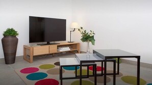 A modern living room with a flat-screen TV, wooden TV stand, a small table with a vase, and a colorful rug. - La Croisette - One Bedroom Apartment, Sleeps 4 (Cannes)