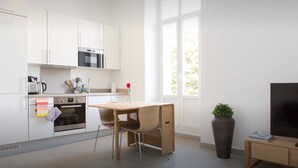 A modern kitchen with white cabinets, a microwave, an oven, and a dining area with a wooden table and chairs. - La Croisette - One Bedroom Apartment, Sleeps 4 (Cannes)