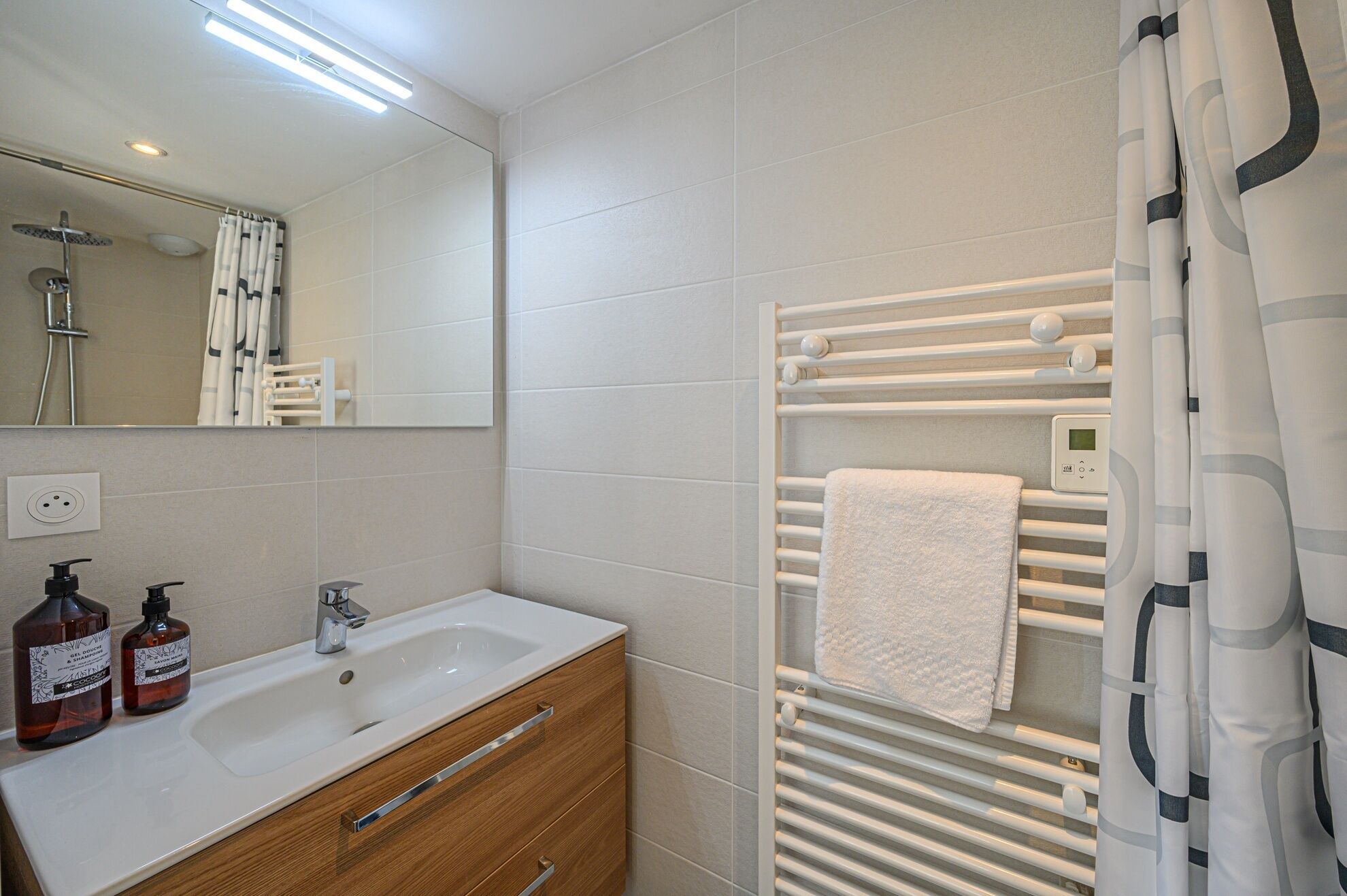 Une salle de bain moderne avec un lavabo blanc, un meuble en bois et un porte-serviettes sur lequel est posée une serviette blanche.