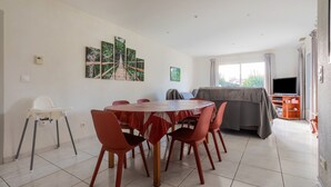 A dining area with a round table, red chairs, and a white high chair. There are wall-mounted paintings and a television in the background. - La Massane - Three Bedroom House, Sleeps 6 (Argeles-sur-Mer)