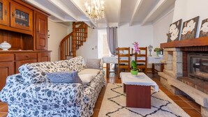 A cozy living room with a floral sofa, wooden cabinets, a fireplace, and a staircase. - L'Orchidée - Two Bedroom House, Sleeps 6 (Limerzel)