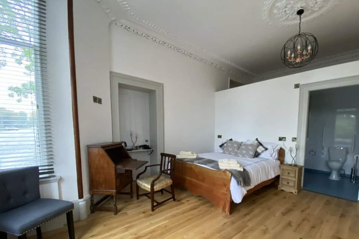 A bedroom with a wooden bed, a desk, a chair, and a window with blinds.