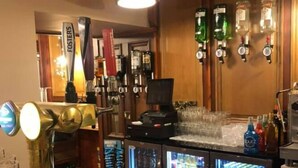Una zona de bar con mostrador de madera, grifo de cerveza y un refrigerador lleno de bebidas.
