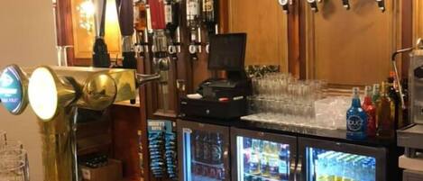 A bar area with a wooden counter, a beer tap, and a refrigerator stocked with beverages.
