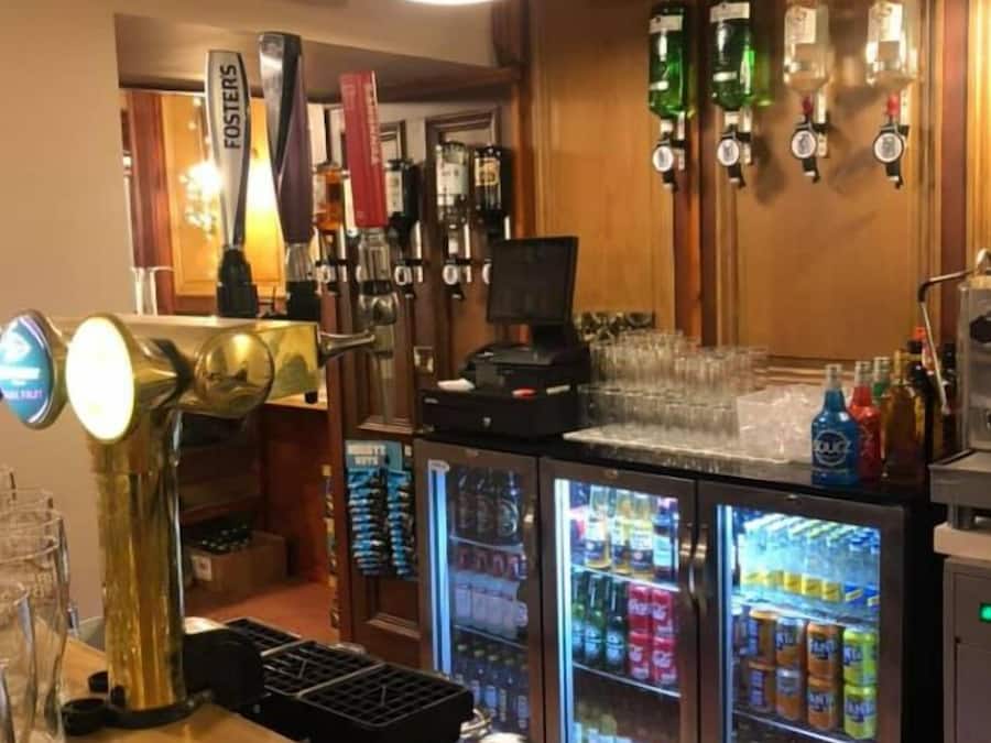 Uma área de bar com balcão de madeira, torneira de cerveja e frigorífico cheio de bebidas.