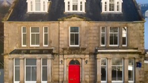 Un edificio histórico de piedra con una puerta central roja, ventanas simétricas y una línea de techo tradicional.
