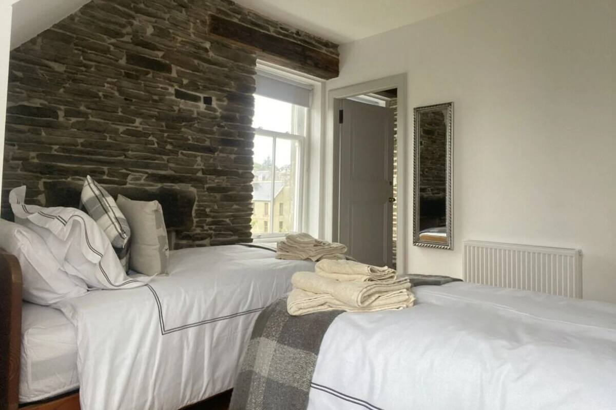A bedroom with two beds, a stone wall, a window, and a mirror.
