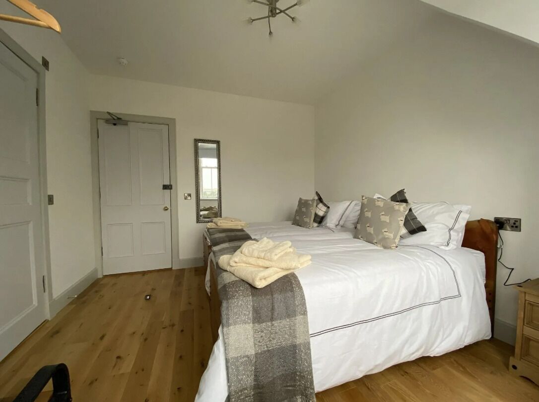 Una camera da letto con un letto grande, pavimento in legno, una porta bianca e uno specchio sulla parete.