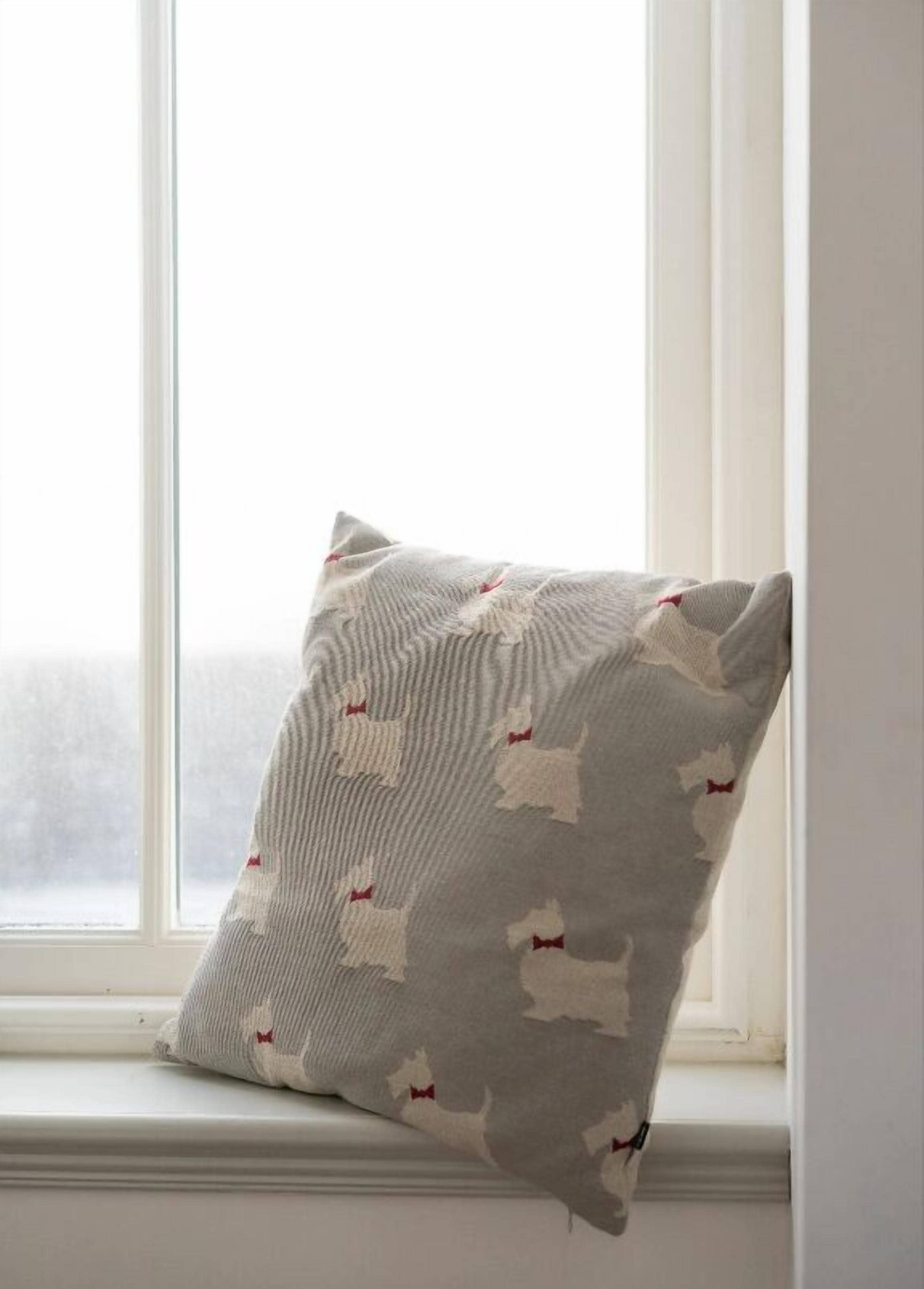 Almohada con un diseño de formas blancas sobre un fondo gris, colocada en un alféizar.