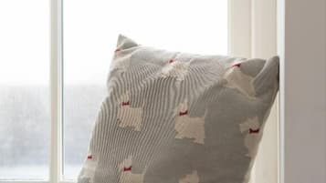 Almohada con un diseño de formas blancas sobre un fondo gris, colocada en un alféizar.