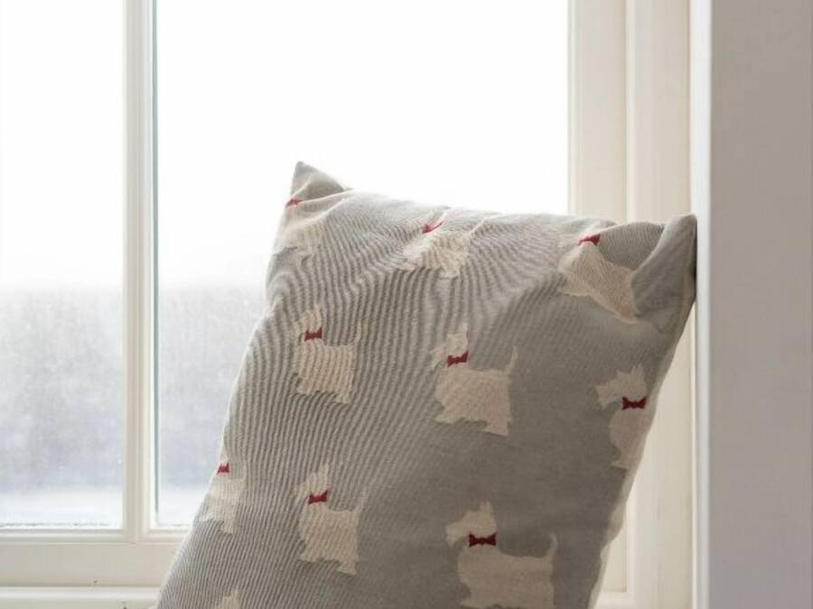 Almohada con un diseño de formas blancas sobre un fondo gris, colocada en un alféizar.