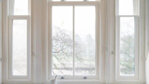 Una habitación con un amplio ventanal arqueado, una pequeña mesa con una taza, y vistas a árboles.