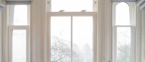 A room with a large arched window, a small table with a cup, and a view of trees outside.