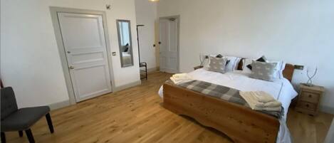 A bedroom with a wooden bed, a chair, a bedside table, and a hanging light fixture.