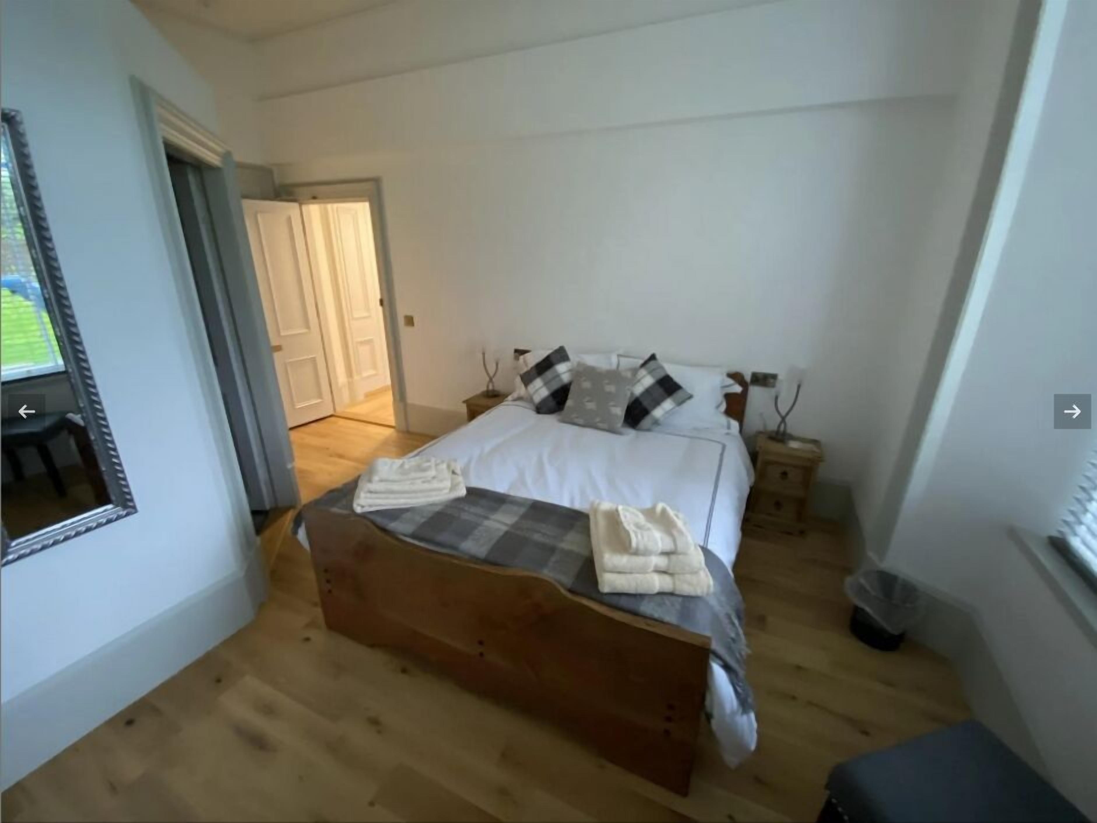Un dormitorio con una cama de madera, ropa de cama blanca y un espejo a la izquierda.