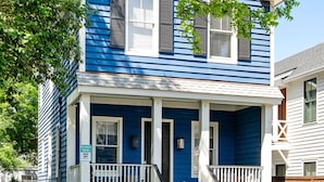 Een blauw huis met twee verdiepingen, een voortuin en een veranda, met een bord dat 'Gereserveerd Parkeren' aangeeft.