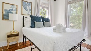 Een keurig opgemaakt slaapkamer met een groot bed, een nachtkastje met een lamp, en twee ingelijste botanische prints aan de muur.