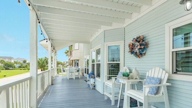 A covered porch with white railings, a seating area with white chairs and a table, and a wreath on the wall. - Spacious Beachside Home w/ Long Gulf View, Covered Deck & Huge Primary Suite (Galveston)