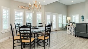 A dining area with a table and chairs, a chandelier, and a sign reading 'BEACH HOUSE'. - Spacious Beachside Home w/ Long Gulf View, Covered Deck & Huge Primary Suite (Galveston)
