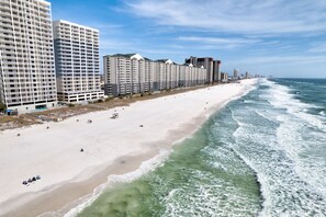 Ein Strandhotel mit mehreren Hochhäusern, einem Sandstrand und Meereswellen.