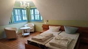Un dormitorio con cama, dos sillas, una mesita, una araña y una ventana con cortinas.