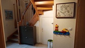 Una escalera con barandillas de madera, un mueble pequeño, una puerta y un estante fijado a la pared con un juguete colorido.