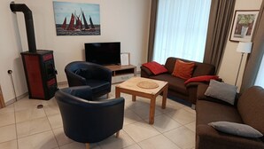 Una sala de estar con sofá, sillón y una mesita. Hay un televisor y una chimenea.