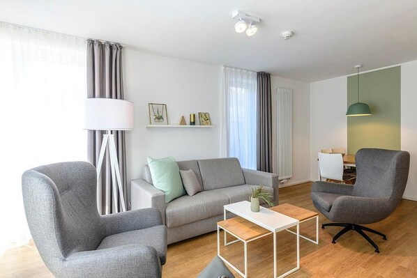 Una sala de estar moderna con un sofá gris, dos sillones grises, una mesa de centro blanca y una lámpara.