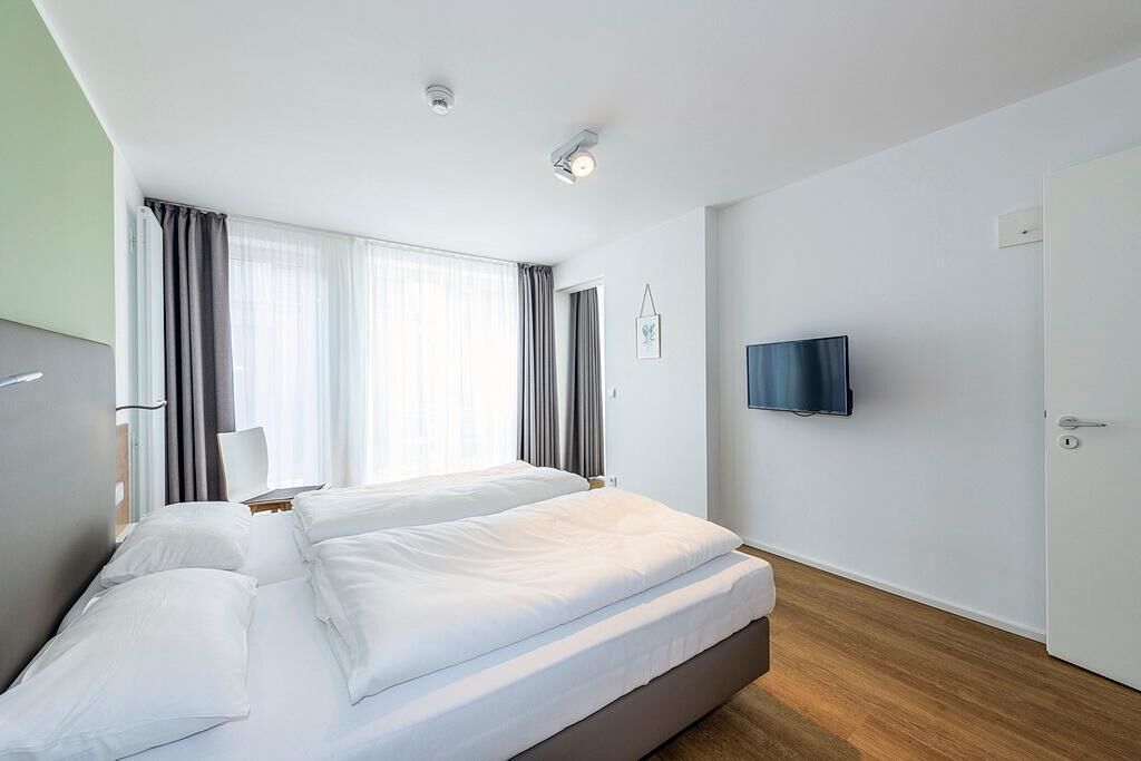 Moderni hotellihuone, jossa on suuri sänky, taulutelevisio ja ovi oikealla puolella.