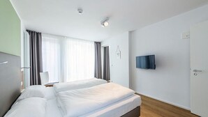 Une chambre d’hôtel moderne avec un grand lit, un téléviseur à écran plat et une porte située sur le côté droit.
