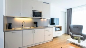 Une cuisine moderne équipée d’un four à micro-ondes, d’un évier et de placards, d’un téléviseur à écran plat et d’un fauteuil gris agrémenté d’une plante.