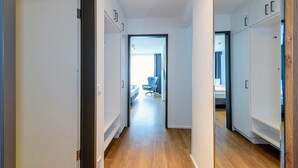 Un couloir étroit, doté d’un plancher en bois, mène à une chambre où se trouvent un lit et une chaise.