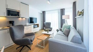 Une chambre d’hôtel moderne équipée d’une kitchenette, d’un canapé gris, d’une table basse et d’un téléviseur.
