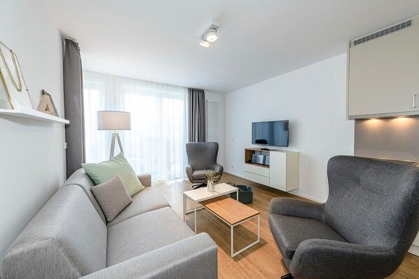 A modern living room with a sofa, armchairs, a coffee table, a TV, and a cabinet.
