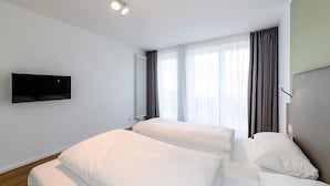 Ein modernes Hotelzimmer mit zwei Betten, einem flachbildfernseher an der Wand und großen Fenstern mit Vorhängen.