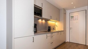 A modern kitchen with white cabinets, a stainless steel range hood, a coffee maker, and a sink.
