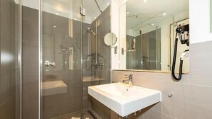 A modern bathroom with a glass-enclosed shower, a white sink, and a large mirror.