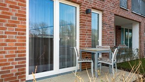A modern brick building with large sliding glass doors, a small patio with a table and chairs, and a visible balcony.