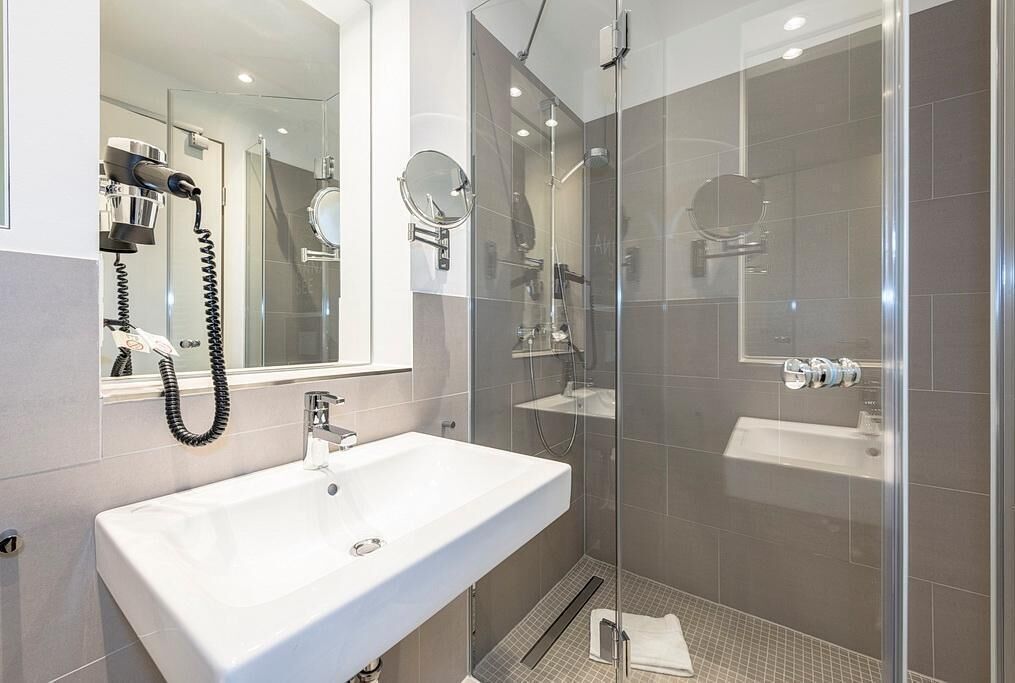 Un baño moderno con un lavamanos blanco, cabina de ducha de vidrio y un secador de pelo de pared.