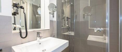 Un baño moderno con un lavamanos blanco, cabina de ducha de vidrio y un secador de pelo de pared.