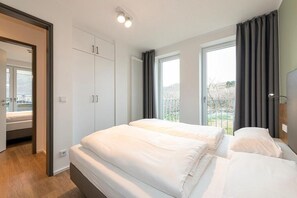 Un dormitorio moderno con dos camas, un armario y un ventanal grande con cortinas.