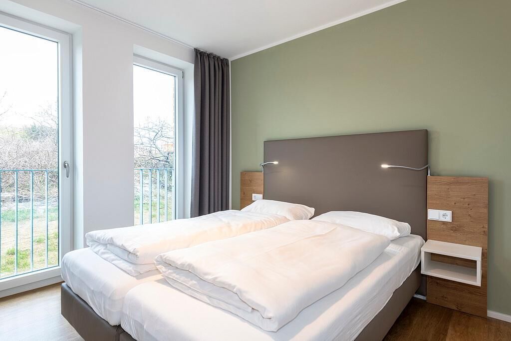 A double bed with a wooden headboard, a bedside table, and a window with curtains.