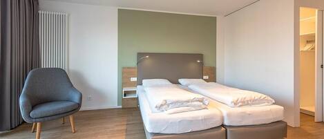 A modern hotel room with a double bed, a grey armchair, and a wooden floor.